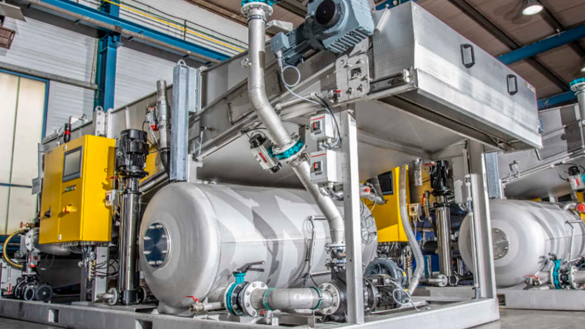 Técnico inspeccionando una planta de tratamiento de aguas residuales modular de color verde marca BIOMAX SYNERTECH, que incluye módulos de pretratamiento, decantación, DAF y oxidación avanzada. La planta está ubicada en un entorno industrial con techo alto y tuberías visibles. - ver más información